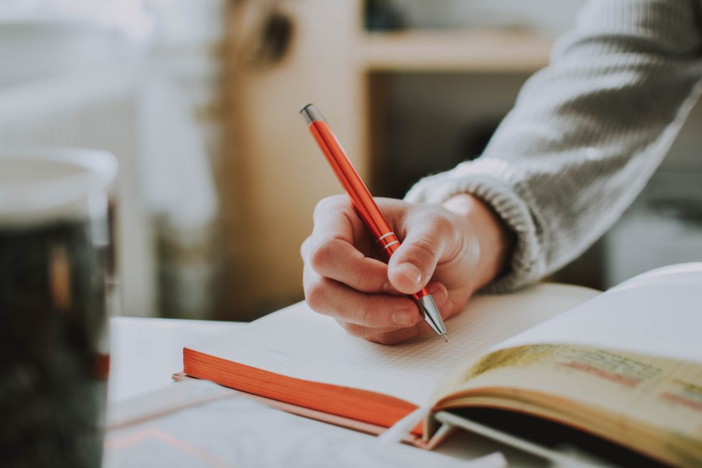 Une personne tenant un stylo et s'apprêtant à écrire dans un cahier